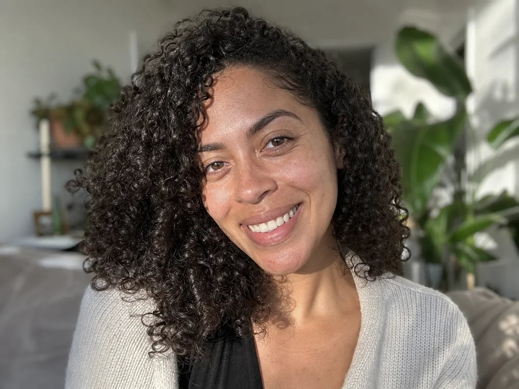 4:3 portrait photograph. A woman with beautifully defined curly hair (type 3B-3C), smiling naturally