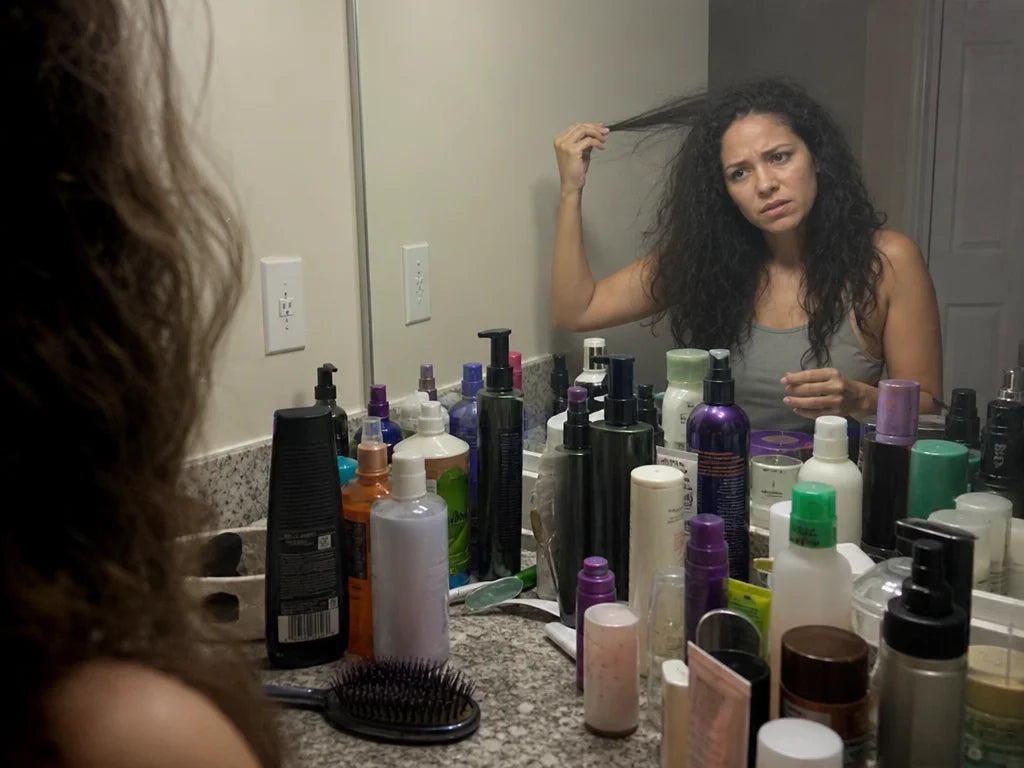 4:3 photograph. A cluttered bathroom counter with many unlabelled generic hair product bottles (vari